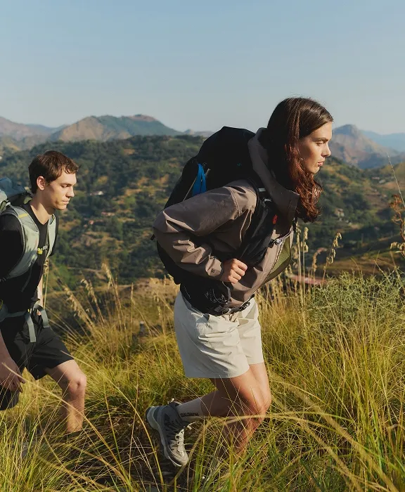 Ein Mann und eine Frau mit Rucksäcken wandern durch eine hügelige Graslandschaft.