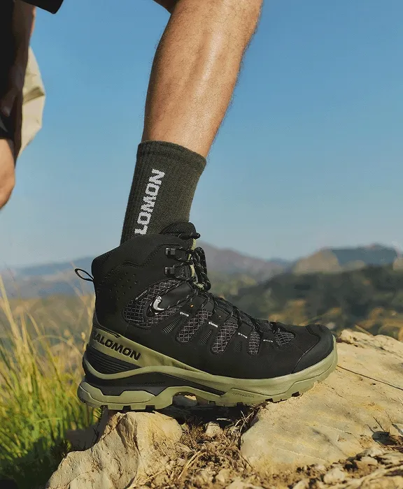 Nahaufnahme eines schwarzen Salomon Wanderschuhs auf einem Felsen vor Gebirgshintergrund.